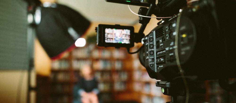 A camera livestreaming a woman giving a presentation in a library