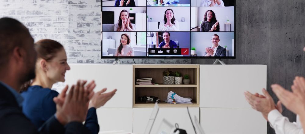 A group of people applauding a live stream they're watching on the conference room monitor.